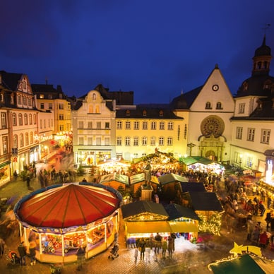 Abendlicher Weihnachtsmarkt auf einem Platz mit Lichtern und Menschen.