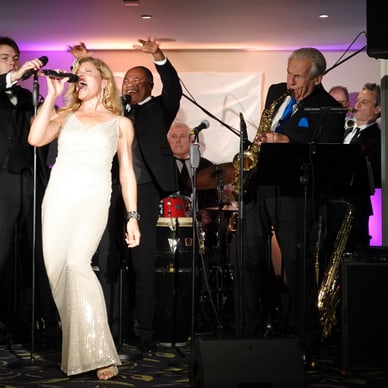Frau in weissem Kleid singt auf Bühne mit Band im Hintergrund.