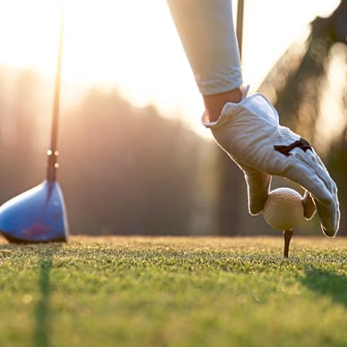 Nahaufnahme einer Hand mit Handschuh, die einen Golfball auf ein Tee setzt.