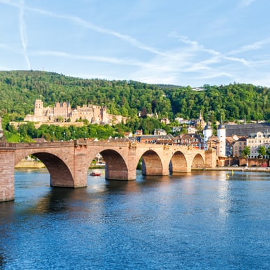 Steinbrücke über einen Fluss mit Stadt und Hügel im Hintergrund.
