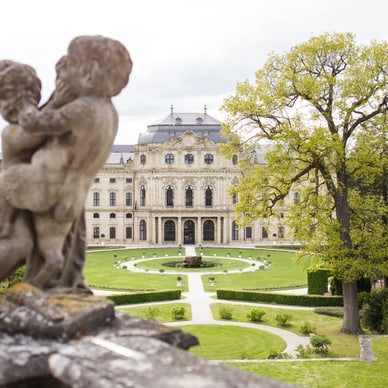 Steinfigur vor barockem Schloss mit Garten.