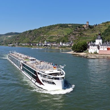 Das Flussschiff Excellence Crown fährt auf dem Rhein, Passagiere auf dem Sonnendeck geniessen den Blick auf Weinberge und historische Gebäude.