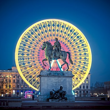 Reiterstatue vor beleuchtetem Riesenrad bei Nacht.