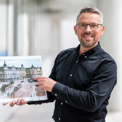 Mann in schwarzem Hemd hält ein Bild in einem Korridor.