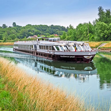 Flusskreuzfahrtschiff auf einem ruhigen Kanal mit grünen Ufern.