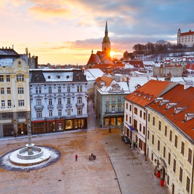 bratislava.jpg Blick auf schneebedeckten Stadtplatz mit historischen Gebäuden bei Sonnenuntergang.