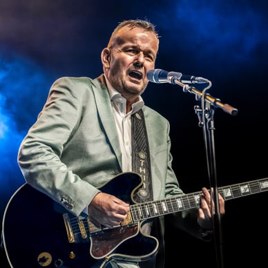 Mann in einem Anzug spielt Gitarre auf einer Bühne.
