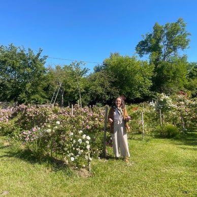 Person in einem Garten mit blühenden Sträuchern und Bäumen unter blauem Himmel.