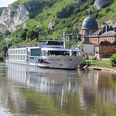 Flusskreuzfahrtschiff auf der Elbe vor malerischer Hügellandschaft.