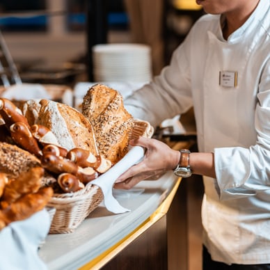 Ein Bäcker in weisser Uniform arrangiert Brot in Körben.
