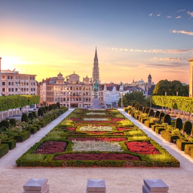 Gartenanlage mit geometrischen Beeten und Stadtblick im Hintergrund bei Sonnenuntergang.
