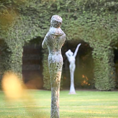 Zwei Skulpturen im Garten vor einer Efeuwand.