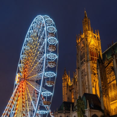 Beleuchtetes Riesenrad neben einer gotischen Kathedrale bei Nacht.