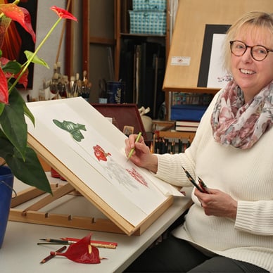 Frau malt Blumen in einem Atelier.