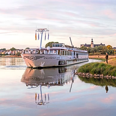 Flusskreuzfahrtschiff auf ruhigem Wasser nahe Ufer und Dorf.