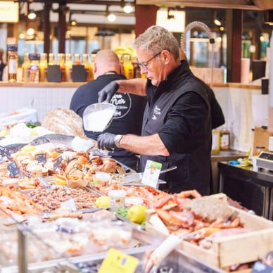 poissonnerie-maison-saiter.jpg Mann hinter einer Fisch- und Meeresfrüchte-Theke auf einem Markt.