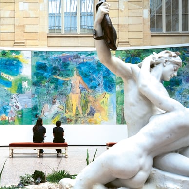Zwei Personen betrachten ein grosses farbenfrohes Gemälde neben einer weissen Statue im Museum.