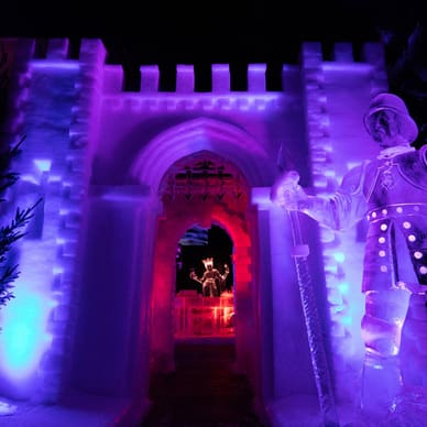 Beleuchtete Eisskulptur eines Ritters vor einem Eistorbogen.