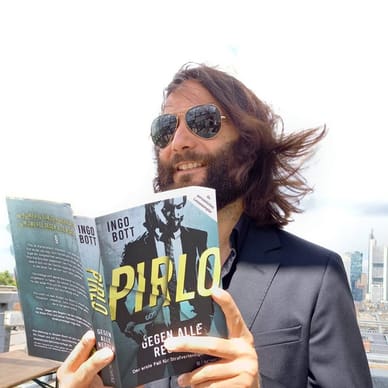 Person mit Sonnenbrille liest Buch auf einer Dachterrasse.