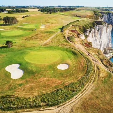 Landschaft mit Küstenklippen, grünen Feldern und Golfplätzen neben dem Meer.