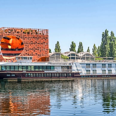 Hausboot auf Fluss, moderne Gebäude im Hintergrund.