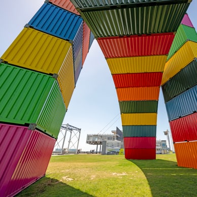 Bogenförmige Skulptur aus bunten Schiffscontainern in Le Havre, Frankreich, vor blauem Himmel.