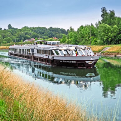 Flusskreuzfahrtschiff auf einem ruhigen Fluss umgeben von Bäumen.