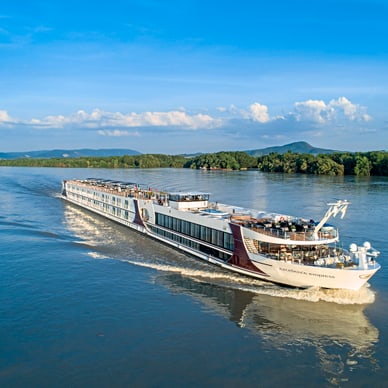 Flusskreuzfahrtschiff auf einem breiten Fluss mit bewaldetem Ufer.