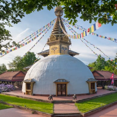 Weisser Stupa mit Gebetsfahnen im Garten.