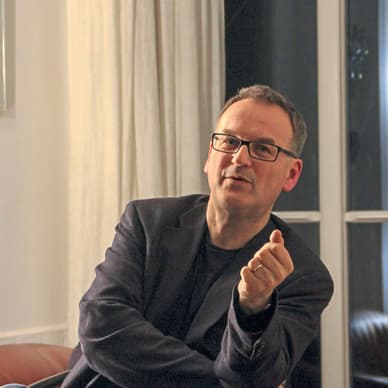 Person mit Brille sitzt auf Sofa und gestikuliert.