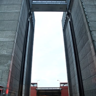Menschen sitzen vor einer hohen Schleusenanlage mit beleuchteter Bühne.
