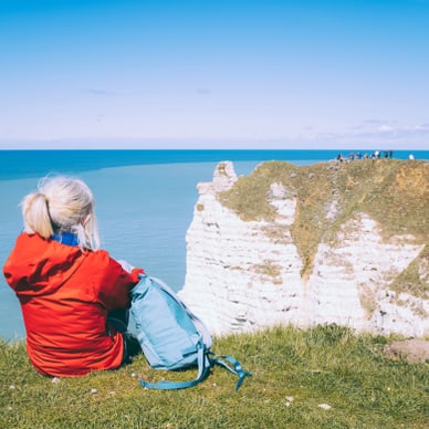 Person in roter Jacke sitzt auf einer Klippe mit Blick auf das Meer.