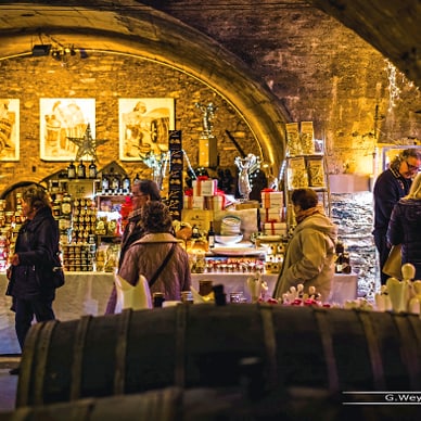 Menschen an einem geschmückten Weihnachtsmarktstand in einem Gewölbekeller.