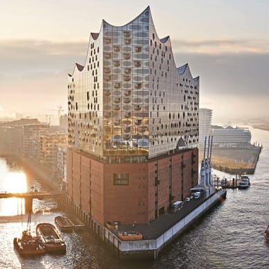 Luftaufnahme der Elbphilharmonie Hamburg mit Glaswellendach über Backsteinbau, Fluss und Brücke im Abendlicht.