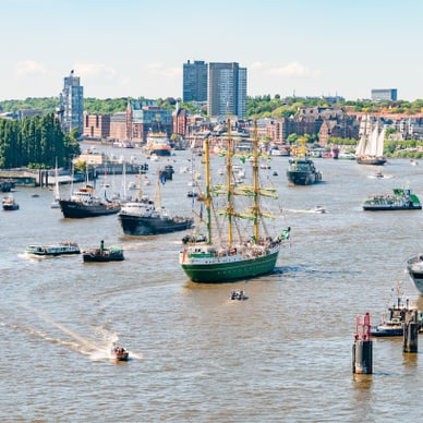 Mehrere Schiffe auf einem Fluss mit Stadt im Hintergrund.