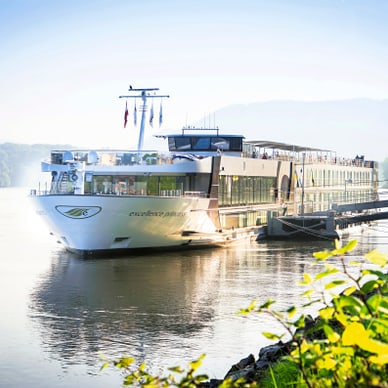Flusskreuzfahrtschiff auf ruhigem Fluss bei sonnigem Wetter.