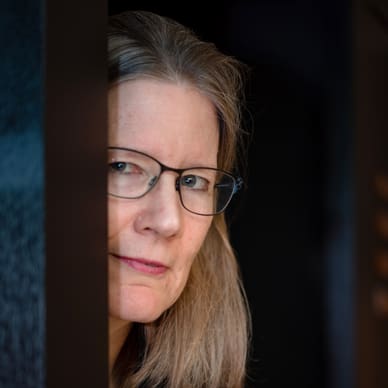 Person mit Brille schaut aus einem Türspalt hervor.