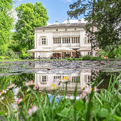 Weisse Villa mit Teich und Blumen im Vordergrund.