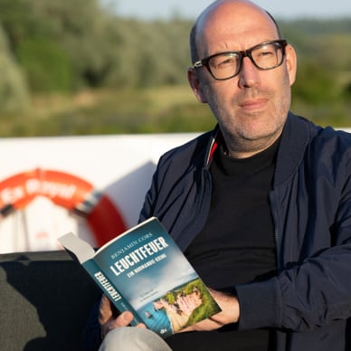 Person liest ein Buch draussen auf einem Boot.