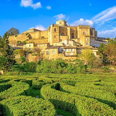 Historische Burg auf einem Hügel mit Labyrinth aus Hecken im Vordergrund.