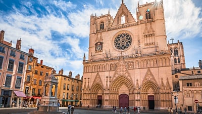 kathedrale-st-jean-lyon.jpg Historische Kathedrale mit Platz und Menschen bei sonnigem Wetter.