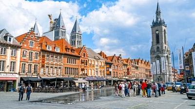 Marktplatz mit historischen Gebäuden, Turm und Menschen, die spazieren.