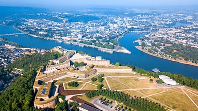 twerenbold_64118.jpg Luftaufnahme einer Festung am Fluss mit Stadt im Hintergrund.