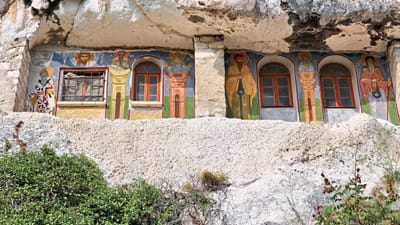 twerenbold_78127.jpg Felswand mit bunten Fresken und Fenstern, von Pflanzen umgeben.