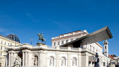 twerenbold_79380.jpg Historisches Gebäude mit Reiterstatue und moderner Dachstruktur unter klarem Himmel.