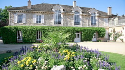 twerenbold_67828.jpg Historisches Steinhaus mit Garten voller Blumen.