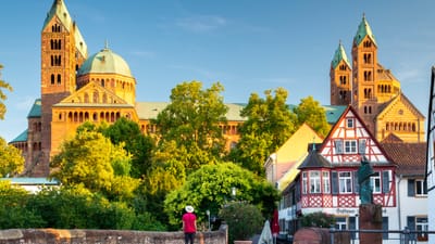 Eine Person auf einem Weg vor einer grossen Kirche und Fachwerkhäusern bei blauem Himmel.