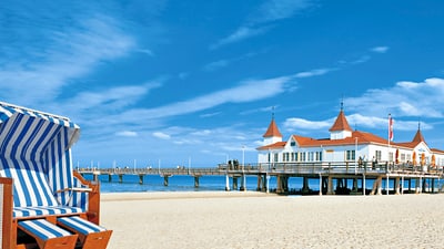 twerenbold_49573.jpg Strandkorb vor Seebrücke und Gebäude am Sandstrand.