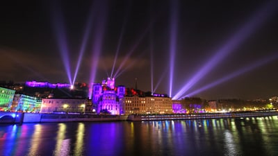 lichterfest-lyon.jpg Nachts beleuchtete Gebäude mit Lichtsäulen am Fluss.