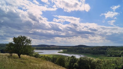 schorheide-chorin.jpg Landschaft mit Fluss, Hügeln und Wolkenhimmel.